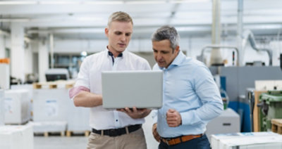  Twee personen die in een open kantoorruimte staan en samen naar een laptop kijken