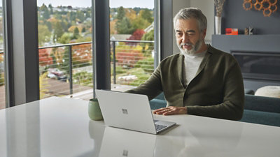 Persona sēž pie virtuves letes, izmantojot klēpjdatoru