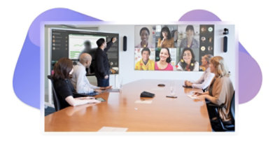 Cinco personas en una sala de reuniones participan en una videollamada de Teams que se visualiza en la pared, y una gran pantalla en el lateral de la sala muestra un PowerPoint y mensajes de la reunión.