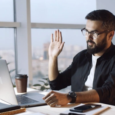 A person waving hello while participating in a Teams video call on a laptop.