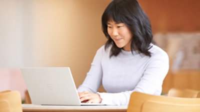 A person sitting at a wooden table smirking and using a laptop.