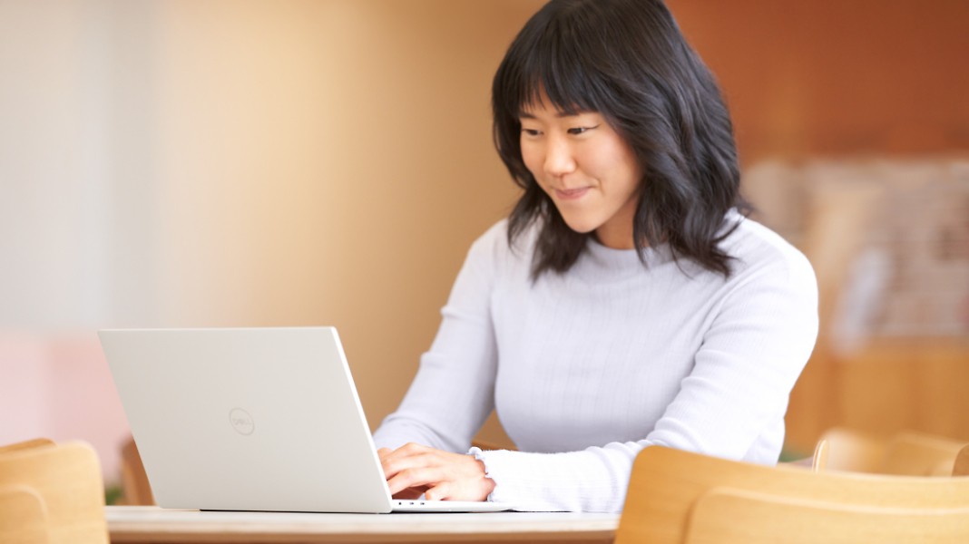 صورة لشخص يجلس على طاولة خشبية يبتسم ويستخدم جهاز كمبيوتر محمول.