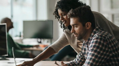Two people working together on a laptop at a desk.