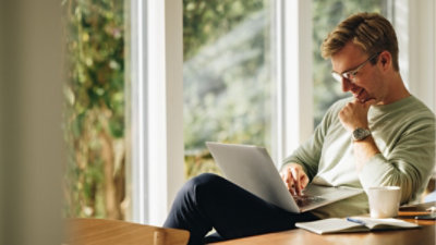 A person sitting in a chair in their home working on a laptop.