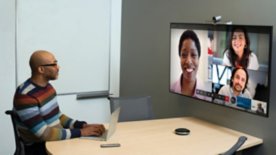 One person sitting in a meeting room taking part in a Teams video call being displayed on a television on the wall with 3 other participants dialed in from other locations.