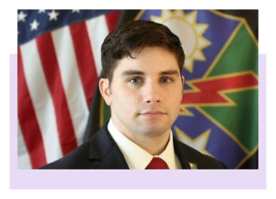 A person in military uniform standing in front of the American flag.
