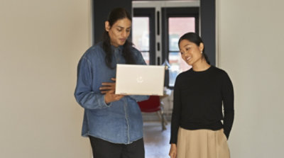 Two people standing outside of a meeting room looking at a laptop
