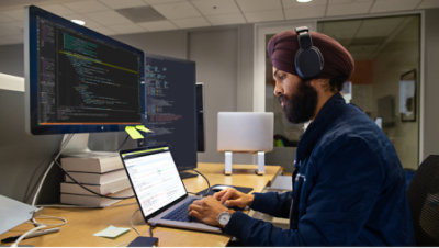 A person wearing headphone and working with multiple screens and laptop