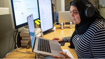 A woman wearing headphone and working with multiple screens and laptop