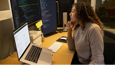 A woman sitting on the chair and working with multiple screens and laptop