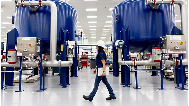 Uma mulher caminha por uma fábrica com filtros de água azuis.