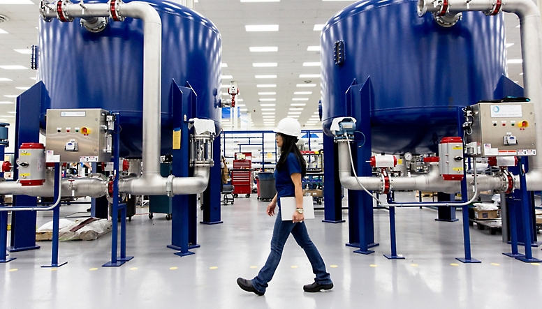 A woman walks through a factory with blue water filters.