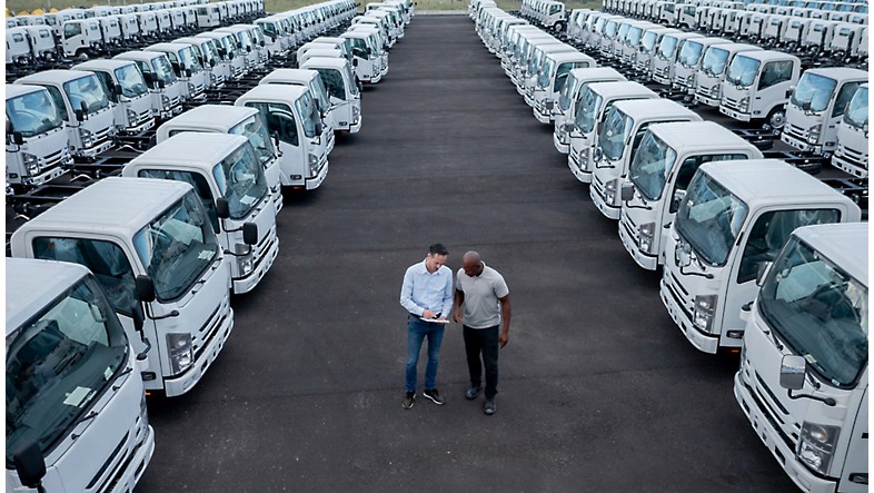 Dos hombres de pie delante de una fila de camiones blancos.
