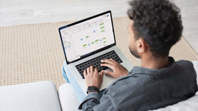 Una persona sentada en un sofá usa una portátil para crear un diagrama intrincado en Visio.