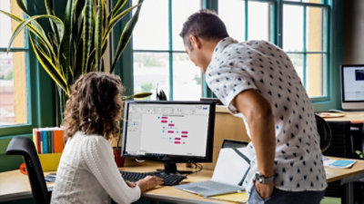 Dos personas observan un monitor de escritorio que muestra un diagrama en Visio.