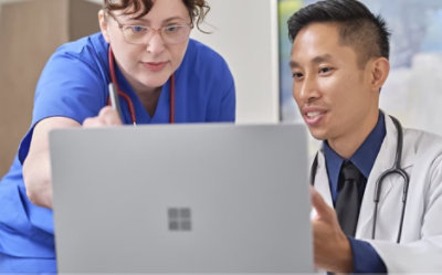 Δύο εργαζόμενοι στον τομέα της υγείας που συνομιλούν και κοιτάζουν έναν φορητό υπολογιστή