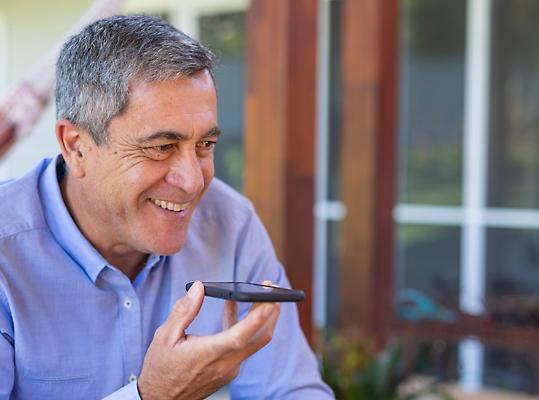Una persona sonríe mientras sostiene un móvil cerca de su boca.