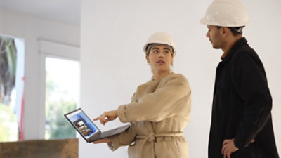 Two people wearing protective hard hats looking at a laptop 