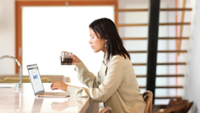 A person holding a coffee mug using a laptop at a kitchen island 