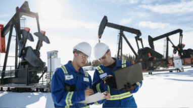 Due persone in un cantiere che indossano indumenti protettivi, usano un computer portatile e guardano dei documenti.