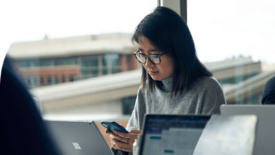 Ένα άτομο που κάθεται στο γραφείο του χρησιμοποιώντας ένα κινητό τηλέφωνο.