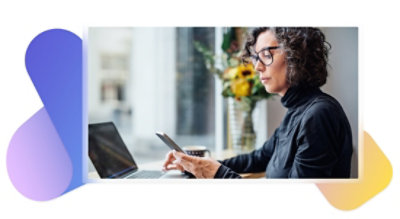 Una persona sentada en su escritorio con un portátil y utilizando un teléfono móvil.