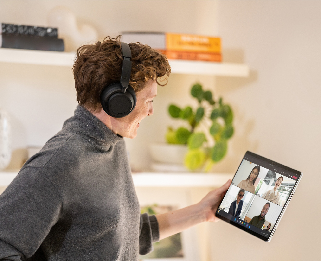 A person wearing over the ear headphones and holding a tablet displaying a Teams video call