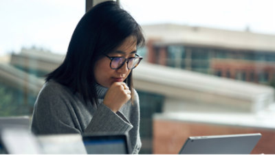 A woman sitting on the chair with her one hand on chin and looking into laptop