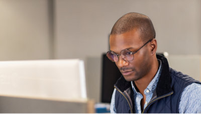 A person wearing spectacles working on his laptop