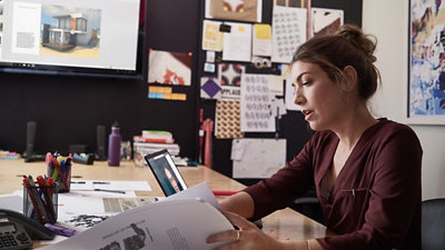 A woman in her office checking some notes while working on the laptop