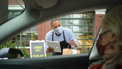 A person wearing a mask delivers a package to a person in a car