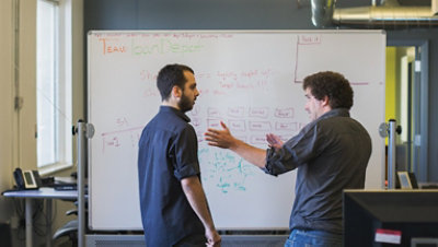 Two people talking in front of a whiteboard
