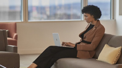 Persona sēž dīvānā un lieto klēpjdatoru