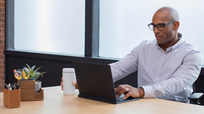 Persona strādā ar klēpjdatoru un tur rokās krūzi