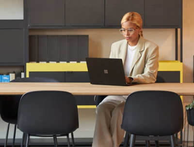 オフィス内で座ってノート PC で作業をしている女性