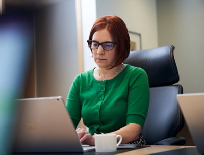 コーヒーを置いたテーブルで、ノート PC で作業している女性