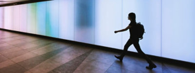 Person, die einen Rucksack trägt und schnell in einem beleuchteten Gang geht.