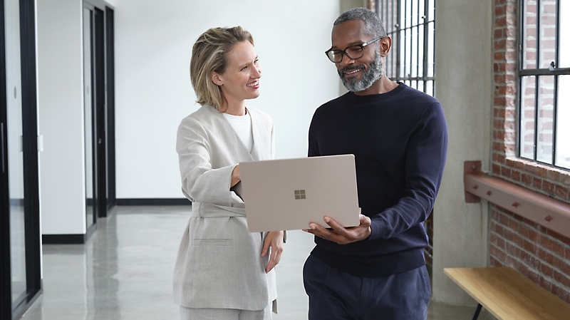Two people in a hallway looking at a laptop and smiling