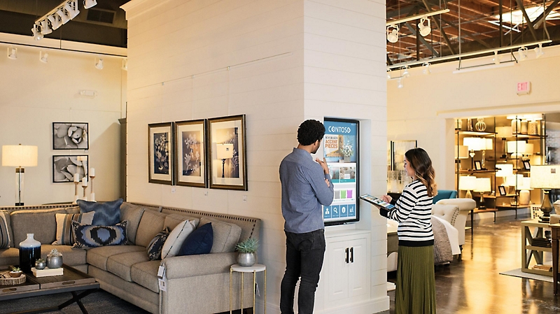 An employee and customer in a furniture store looking at a video wall displaying product information