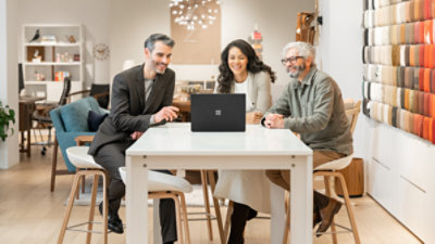 Three people sitting at a hightop table looking at a laptop