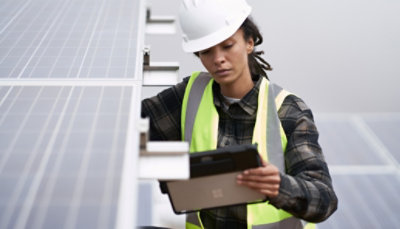 A woman working on a solar panel with a tablet.