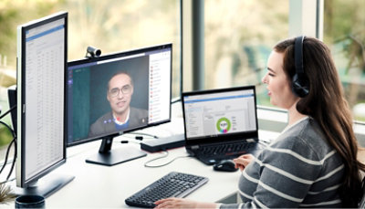 A woman sitting at a desk with two monitors, laptop and a headset.