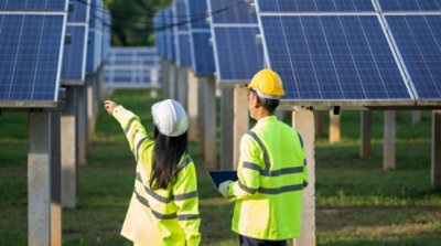 안전 조끼와 안전모를 착용한 두 명의 작업자가 태양광 패널을 살펴보고 있습니다.