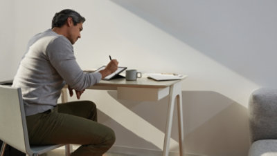 Persona sēž pie galda, izmantojot pildspalvu un planšetdatoru