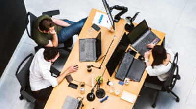 A top-down view of three people sitting at back-to-back desks working on laptops 