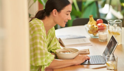A woman sitting at a table with a laptop and bowl of food.