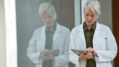 A person leaning against a glass wall using a tablet