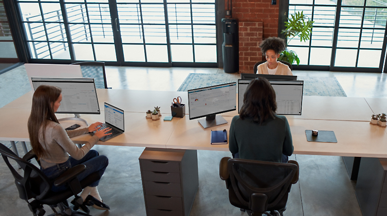 Three people working at their desks next to each other in an open office environment