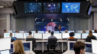 An office with long rows of people working at desks and screens on the wall displaying data