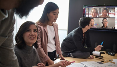 Eine Person nimmt an einem Microsoft Teams-Videochat teil, während drei junge Frauen sich über die Arbeit unterhalten.